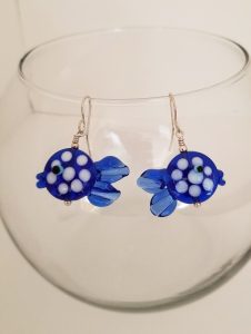 Stone blue fish earrings hanging on clear glass lip