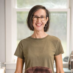 Woman wearing glasses, short brown hair and green tee shirt smiling